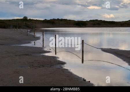 Sandiger Weg rund um den See an stürmischen Tagen, Sturmwolken, Holzplanke, Spiegelungen im Wasser Stockfoto