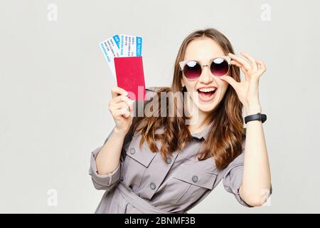 Mädchen in Sonnenbrille hält einen Pass und Tickets lächelnd an der Kamera. Nahaufnahme. Stockfoto