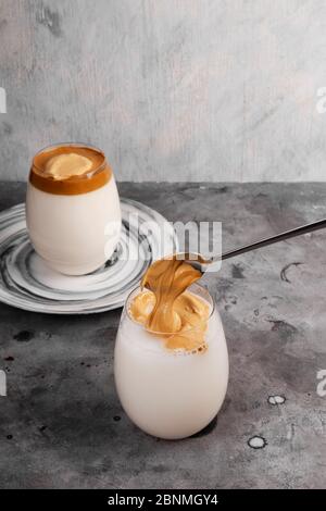 Beliebte Getränk koreanischen Dalgon Kaffee. Langer Löffel fügen Sie üppigen Schlagschaum auf Glas Milch auf grauem Hintergrund Stockfoto