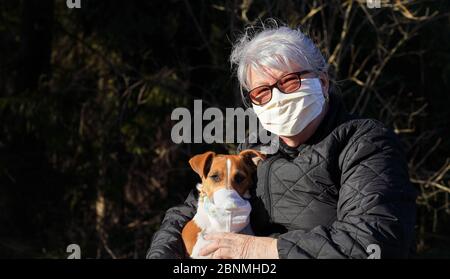 Ältere ältere ältere Frau trägt Virusmaske im Park mit ihrem Hund in einem einfachen Atemschutzgerät. Haustiere sind nicht anfällig für Coronavirus Covid-1 Stockfoto