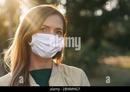 Junge Frau trägt weiße Baumwolle Virus Mund Nasenmaske, schöne Bokeh im Hintergrund, Nahaufnahme Gesicht Porträt Stockfoto