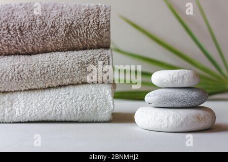 Drei graue Rundsteine und Badetücher auf weißem Hintergrund mit grünen Blättern. Spa-Steine, Zen-Konzept. Stockfoto