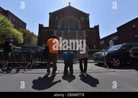 New York City, USA. Mai 2020. Die Menschen beten außerhalb der römisch-katholischen Kirche der Saint Bartholomew Parish während Gottesdiensten, die über einen Lautsprecher stattfinden, während die Menschen Nahrungsmittelhilfe erhalten, im Stadtteil Elmhurst des New Yorker Stadtbezirks Queens, NY, 15. Mai 2020. Catholic Charities Brooklyn und Queens bieten kostenlose Lebensmittel in der Kirche aufgrund der zunehmenden Unsicherheit von Lebensmitteln aufgrund der Auswirkungen von COVID-19 auf die Wirtschaft, wo 1600 Essenskarten wurden an Menschen, die in der Schlange warten, so früh wie 3 Uhr morgens, Jeder bekam Beutel mit genügend Essen, um etwa elf Mahlzeiten zu machen. Stockfoto