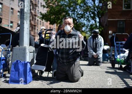 New York City, USA. Mai 2020. Ein Mann, der wegen der COVID-19-Pandemie eine Gesichtsmaske trägt, kniet auf dem Bürgersteig nieder, während er außerhalb der römisch-katholischen Kirche der Saint Bartholomew Parish bei Gottesdiensten über einen Lautsprecher betet, während die Menschen Nahrungsmittelhilfe erhalten, im Stadtteil Elmhurst des New Yorker Stadtbezirks Queens, NY, 15. Mai 2020. Stockfoto