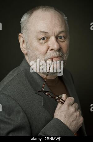 Älterer Mann mit Brille, Bart und Glatze schaut glücklich auf die Kamera Stockfoto