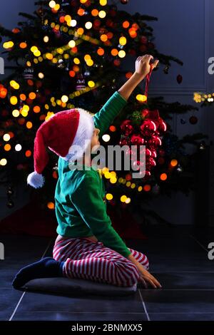 Happy Little Kind Junge schmücken Weihnachtsbaum sitzen in festlichen Kostüm der Elfe am Abend Stockfoto