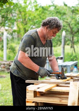 Reife kaukasische Mann hämmern einen Nagel in ein Brett in einem Garten Stockfoto