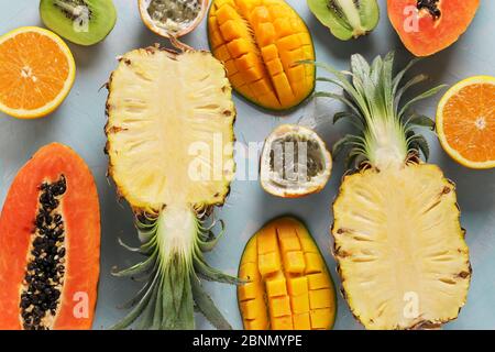 Hälften tropischer Früchte: Papaya, Mango, Ananas, Kiwi, Orange und Passionsfrucht auf hellblauem Hintergrund, Draufsicht Stockfoto