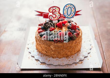 Himbeeren Brombeere Geburtstagstorte mit Kerzen Nummer 30 auf defokussierten Hintergrund mit Holztisch. Makroaufnahme mit selektivem Fokus und flachem Freiheitsgrad Stockfoto