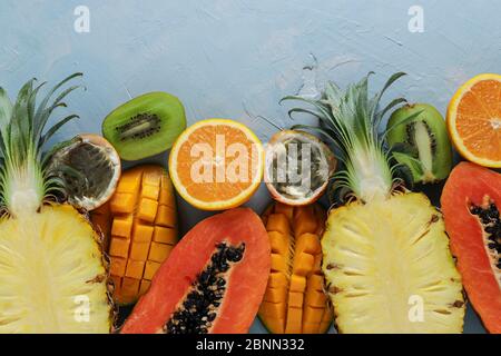 Hälften tropischer Früchte: Papaya, Mango, Ananas, Kiwi, Orange und Passionsfrucht auf hellblauem Hintergrund, Draufsicht, Nahaufnahme Stockfoto