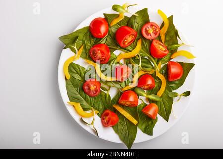 Salat mit Basilikumblättern, Kirschtomaten und Paprika auf weißem Teller. Blick von oben. Stockfoto
