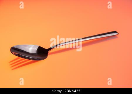 Metalllöffel wirft einen Schatten der Gabel auf orangefarbenem Hintergrund Stockfoto