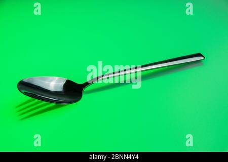 Metalllöffel wirft einen Schatten der Gabel auf grünem Hintergrund Stockfoto