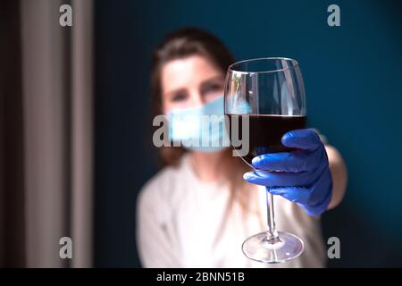 Frau mit Schutzmaske und blauen Handschuhen in ihrem Haus und trinken Rotwein, selbstisoliert für Coronavirus Covid-19, traurig und einsam Stockfoto