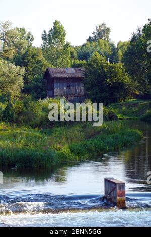 Staudamm am Fluss im Hintergrund eine historische, hölzerne Wassermühle. Stockfoto