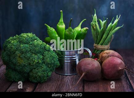 Grüner Paprika in emaillierter Gießkanne, Brokkoli und Rüben auf dunklem Holzhintergrund. Stockfoto