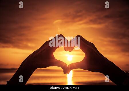 Hand geformtes Herz bei Sonnenuntergang am Meer Stockfoto