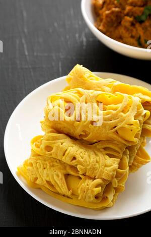 Hausgemachte Net Crepe Roti Jala auf einem weißen Teller auf einer schwarzen Oberfläche, niedrige Winkel-Ansicht. Stockfoto