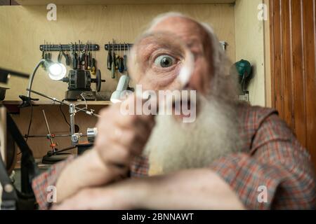 Älterer alter Mann, der durch eine Lupe schaut. Lustige ältere Erstaunen Untersuchung alter Mann Messer schärfen Meister Beruf Stockfoto