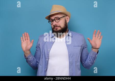 Bärtiger Mann in Sommerhut und Brille Hände in Stop Geste sagen, es war nicht ich. Studio auf blauer Wand gedreht. Stockfoto