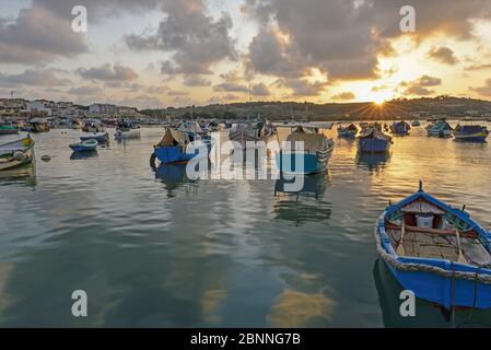 Sonnenaufgang im Fischerhafen von Marsaxlokk mit den typischen bunten Fischern im Vordergrund Stockfoto