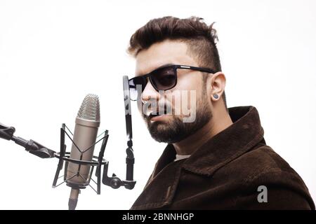 Begabten jungen Mann, der eine braune und eine Brille Mantel ein Lied singen im Studio Aufnahme Stockfoto