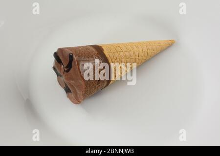 Schokoladeneis-Konus mit Fudge-Belag auf weißem Teller Stockfoto
