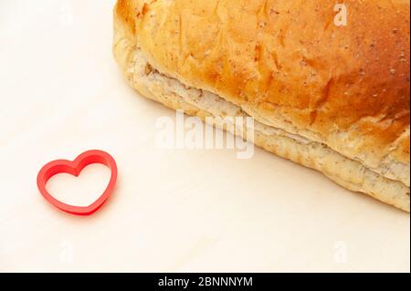 Brasilianisches hausgemachtes Brot neben einem roten Herzobjekt. Isoliert auf hellem Holzhintergrund. Kopierbereich. Stockfoto