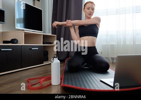 Das Mädchen ist in Stretching Hände zu Hause beschäftigt, sitzt vor einem Laptop Stockfoto