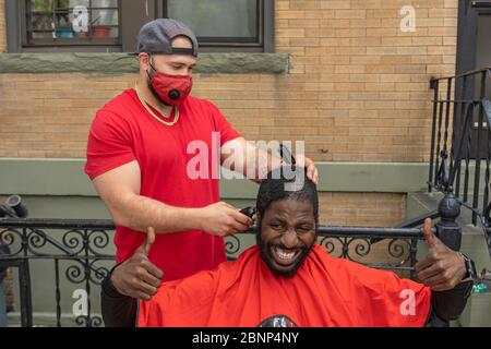 NEW YORK, NY - 15. MAI 2020: Ein Mann bekommt einen Haarschnitt von einem Friseur auf dem Bürgersteig inmitten der COVID-19 Pandemie. Stockfoto