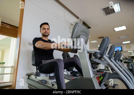 Ganzkörperaufnahme eines jungen bärtigen Indianers, der Cardio-Übungen im Fitnessstudio macht Stockfoto