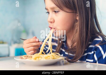 Das Kind isst eifrig leckere Pasta in der Küche Stockfoto