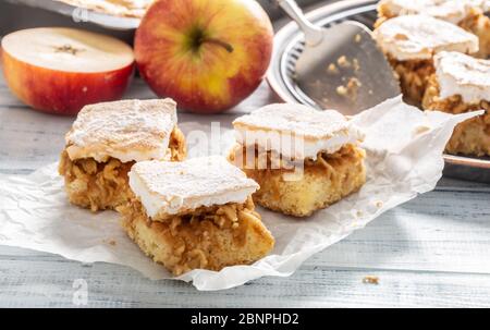 Drei Würfel Apfelkuchen mit einem geschlüpften wgg Weiß Belag auf einer Serviette mit mehr Kuchen und frischen Äpfeln in der Rückseite. Stockfoto