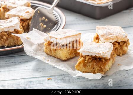 Drei Würfel Apfelkuchen mit einem gewissten wgg Weiß, das auf einer Serviette mit mehr Kuchen im Rücken umtoppen. Stockfoto