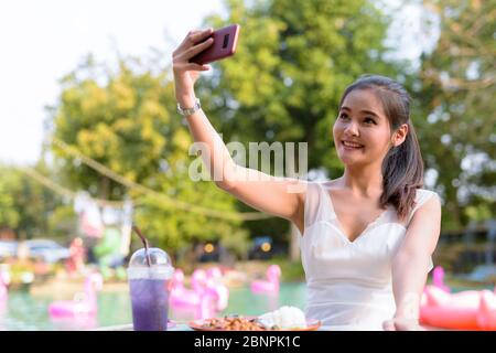 Glücklich junge schöne asiatische Frau unter Selfie im Freien Stockfoto