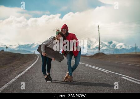 Zwei glückliche junge Mädchen stehen mit Longboards an der Bergstraße und haben Spaß