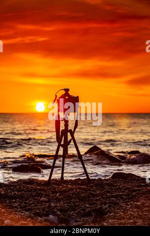 Fotokamera auf Stativ bei Sonnenuntergang am Meer Stockfoto