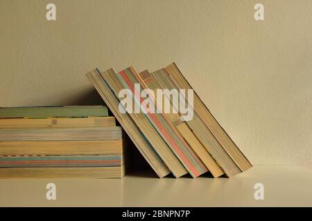 Selektiver Fokus auf eine Reihe von Büchern in vertikaler Position, die sich gegen einen Stapel Bücher auf einem weißen Tisch mit Sonnenlicht und Schatten lehnt Stockfoto