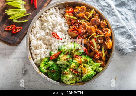 Draufsicht auf ein Teriyaki-Huhn mit Reis, Brokkoli und Chili auf einem weißen Tisch. Stockfoto