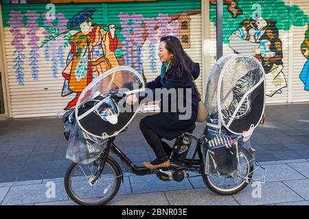 Japan, Honshu, Tokio, Asakusa, Frauen, die auf dem Kinderfreundlichen elektrischen Zweirad Radfahren Stockfoto