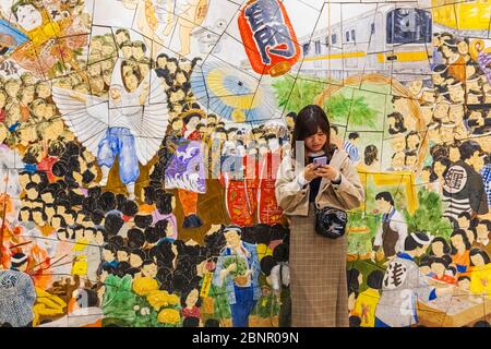 Japan, Honshu, Tokio, Asakusa, Ginza Subway Line, Asakusa Station, Junge Frau, die vor Mosaik steht und Volksfeste darstellt Stockfoto