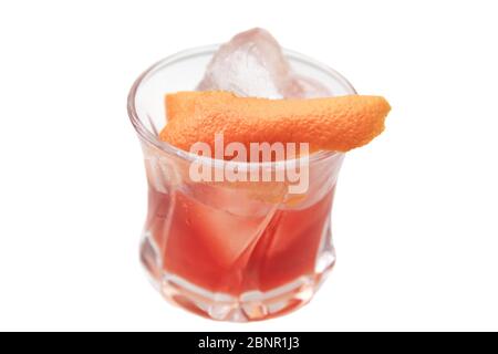 Rötlich-brauner Cocktail in einem Felsglas auf einem isolierten weißen Hintergrund. Der Cocktail wird mit einem orangen Twist und handgeschnittenem Eis garniert. Stockfoto