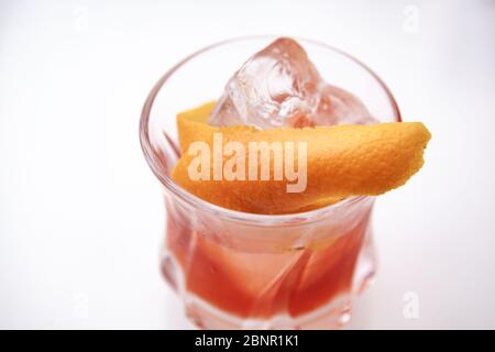 Rötlich-brauner Cocktail in einem Felsglas auf einem isolierten weißen Hintergrund. Der Cocktail wird mit einem orangen Twist und handgeschnittenem Eis garniert. Stockfoto