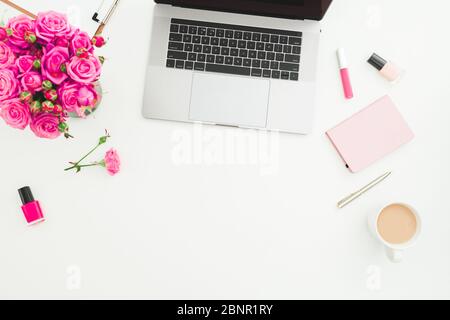 Schreibtisch für das Home Office. Weiblicher Arbeitsplatz mit Laptop, Rosenstrauß, Kosmetik und Tagebuch auf weißem Hintergrund. Flaches Lay. Draufsicht. Stockfoto