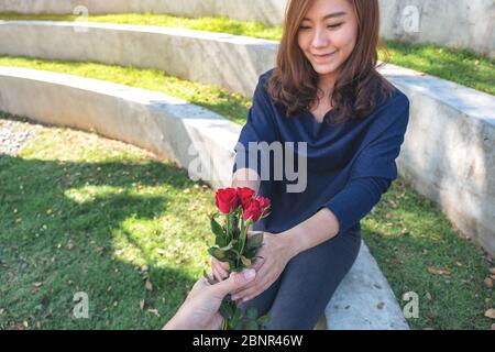 Eine schöne asiatische Frau, die rote Rosenblüten vom Freund am Valentinstag im Freien erhält Stockfoto