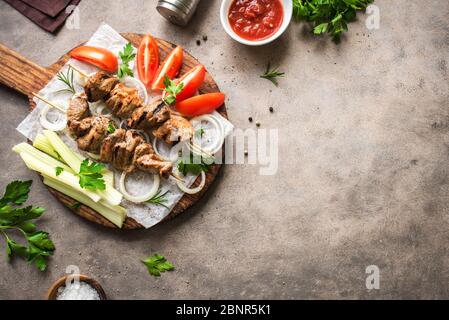 Gegrilltes Schweinefleisch Kebabs auf Spieße auf dunklem Hintergrund, Draufsicht, Kopierraum. Fleisch Schweinefleisch, Huhn oder putenschisch Kebab mit Gemüse, Kräutern und Gewürzen. Stockfoto