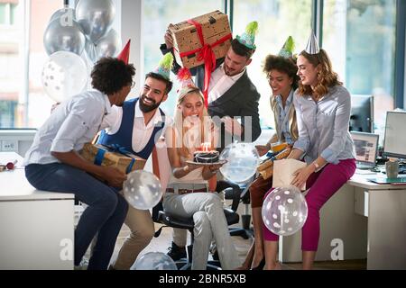 Überraschung Geburtstagsfeier im Büro. Glückliche Mitarbeiter feiern mit Ballonen, Geschenken und Kuchen. Thema der Büroparty. Stockfoto