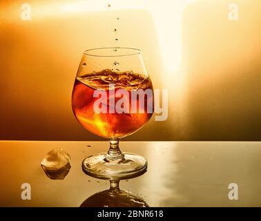 Glas Whiskey mit Tropfen und Eis auf orangefarbenem Hintergrund. Glas Whiskey und Tropfen Symbol Design. Stockfoto
