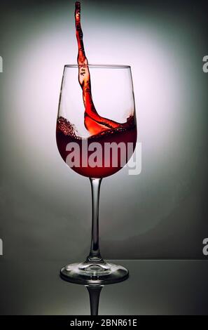Glas Rotwein mit Welle auf grauem Hintergrund. Weinglas und Spritzsymbol. Stockfoto