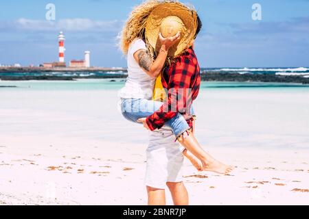 Pärchen küssen mit Liebe - Konzept der Sommerferien Urlaub oder Flitterwochen für Menschen in Beziehung - Hintergrund mit Strand und blauem Meer und Himmel - Mann tragen Frau mit lockigen Haaren Stockfoto